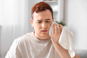 Young man with cold compress suffering from toothache in living room
