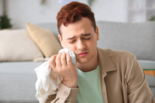 Young man with cold compress suffering from toothache in room