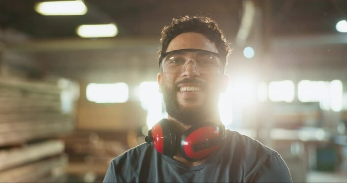Man, carpenter and face in workshop or factory for wood production, manufacturing and trade in safety gear. Young industry worker with smile, confidence and portrait for artisan career in warehouse