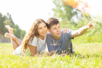Fototapeta premium Happy couple lie on green grass point with hand to something
