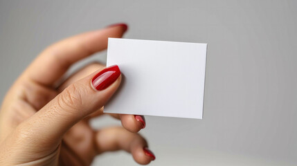 Obraz premium A hand holding a white business card with a red nail polish. The card is rectangular and has a clean, professional look