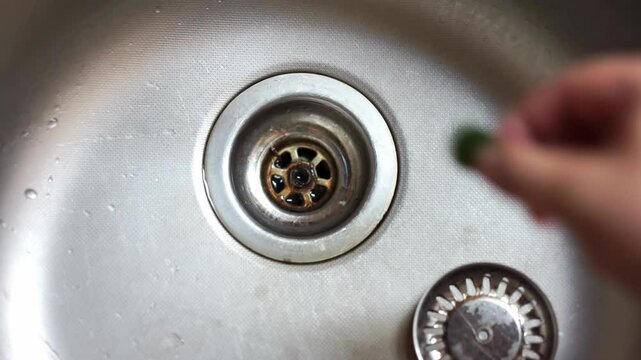 Hand removes anti-clog nozzle from steel sink, pulls out a piece of scouring sponge, prevents blockage of drain hole Plumbing cleaning, dirt, rust, plaque Close-up of a kitchen sink with leftover food