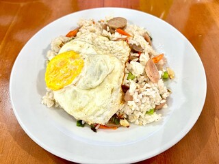 Top view or flat lay shot of homemade Indonesian Fried Rice or Nasi Goreng with meatballs, sausage, and sunny side up egg on a plate