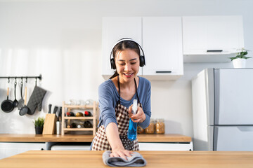 Asian young woman cleaner wearing headphones cleaning kitchen at home.