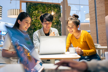 Group of Asian friends talking and using laptop computer in restaurant. 