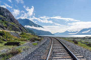 Railroad tracks running through Alaskan landscape with mountains and blue sky
