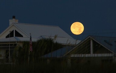 The glowing full moon hovering over a house at the beach in Florida