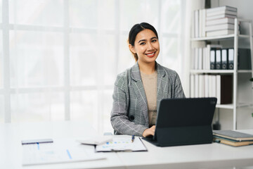 Confident Asian Business Woman Working on Laptop in Modern Office Setting with Documents and Books
