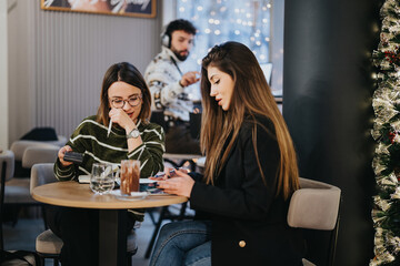 Friends enjoying a cozy evening at a cafe decorated for Christmas, sharing moments together.