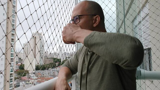 48 year old Brazilian, with glasses, on the balcony of the building drinking coffee.