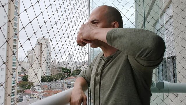 48 year old Brazilian, serious, on the balcony of the building drinking coffee.