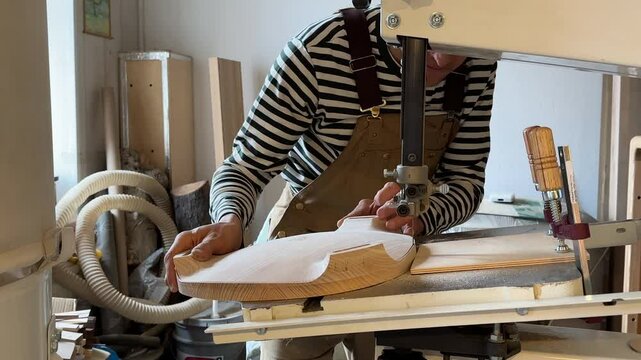 Carpenter man cuts out a chair top with an electric jig saw. Carpentry workshop. Focused guy joiner carved on wood with help of sabre saw machine. Concentrated male working at machine.