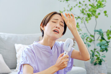 蒸し暑いリビングで携帯扇風機を使う女性