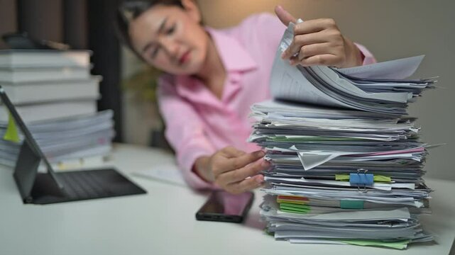 Professional sorting stacks of documents at a desk in an office environment. Person struggling with paperwork, surrounded by laptop, stationery, and books