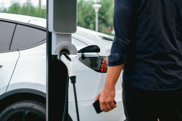 Man using smartphone online banking application to pay for electric car battery charging from EV...