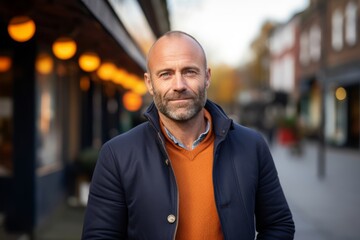 Fototapeta premium Portrait of a handsome middle-aged man with a beard and mustache in an orange jacket on the street.