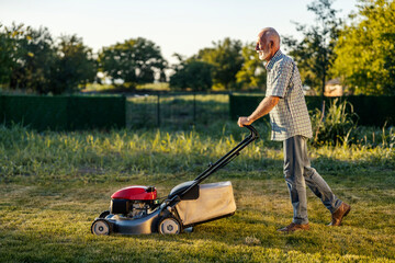 Side view of senior man mowing lawn in his backyard.