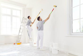 Team of professional male painters painting a white wall in empty room with paint roller. Building...