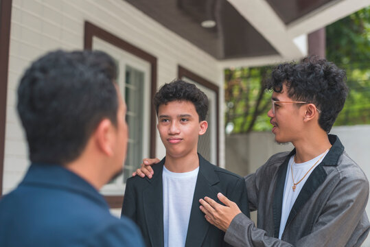 An Asian man teases his son alongside his brother. The son responds with a sarcastic expression while standing outside a house.