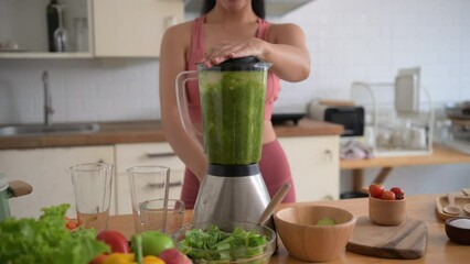 Woman blends a healthy green smoothie in a modern kitchen. Fresh lettuce and fruits are on the counter, creating a nutritious and delicious drink