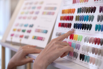 Close up female hands are choosing nail polish color from different fashion color charts, colorful chart of nail polish colors is displayed in beauty shop