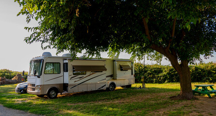 Rv motorhome parked at campsite under trees exscaping the California summer sun and heat