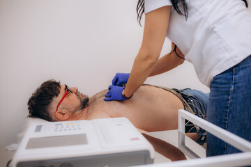 Doctor cardiologist is attaching vacuum sensors to an elder senior patient for recording ECG or EKG...