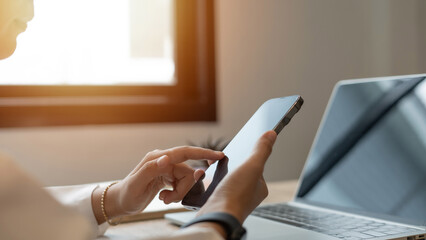 Fototapeta premium A woman is using a tablet and laptop computer at her desk. She is looking at the screen and touching the tablet