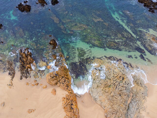 Coast of desert island with blue turquoise water beats on rocky reef. Aerial top view.