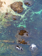 Coast of desert island with blue turquoise water beats on rocky reef. Aerial top view.