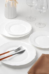 Stylish table setting with white dishware on white tablecloth