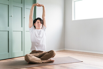 家でヨガ・ピラティス・瞑想・マインドフルネスする若いアジア人男性
