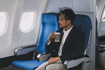 Satisfied millennial businessman drinking coffee, enjoying comfortable flight while sitting in airplane cabin.
