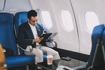 Handsome businessman checking email on laptop while sitting comfortable seat in aircraft cabin during flight.