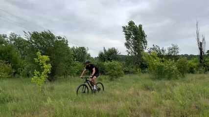Man biking through grassy field surrounded by trees under cloudy sky. Outdoor adventure and physical activity in nature