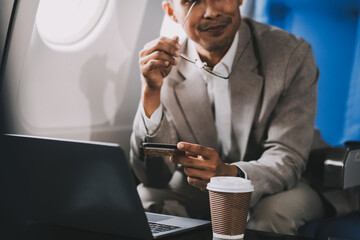 Businessman holding credit card and looking at camera near laptop in private jet