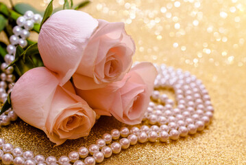 Pink rose and pearl necklace on a shiny gold background
