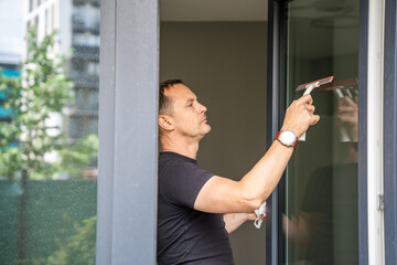 Young man cleans the windows in the house. He splashes detergent, rubs and removes water at the glass