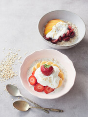 stylish pink bowl of oat porridge with yogurt, banana and strawberries on the gray table, ready to taste with an old-fashioned spoon