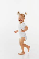 First steps. Cute little child, baby girl in white body running and laughing against white studio background. Positive emotions. Concept of childhood, motherhood, care, life, birth. Copy space.