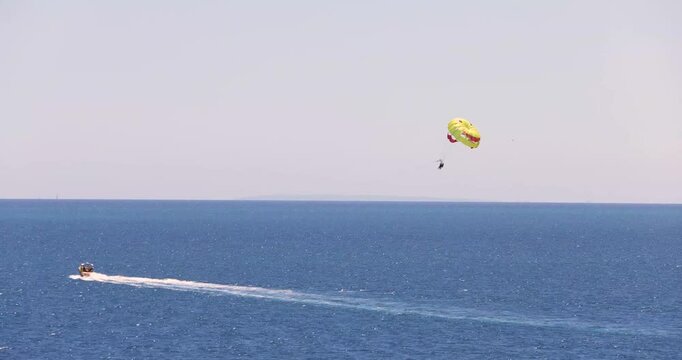 Footage of a Parasailer who is Parasailing over the ocean in the city of Benidorm in Spain showing the glider being pulled by a speed boat