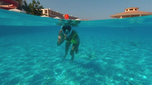 A beautiful girl swims underwater in a pool wearing a mask on a hot sunny day. underwater view