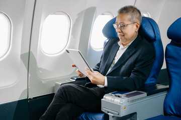 Asian Mature man sitting in a seat in airplane and looking out the window going on a trip vacation travel concept. using a phone, laptop