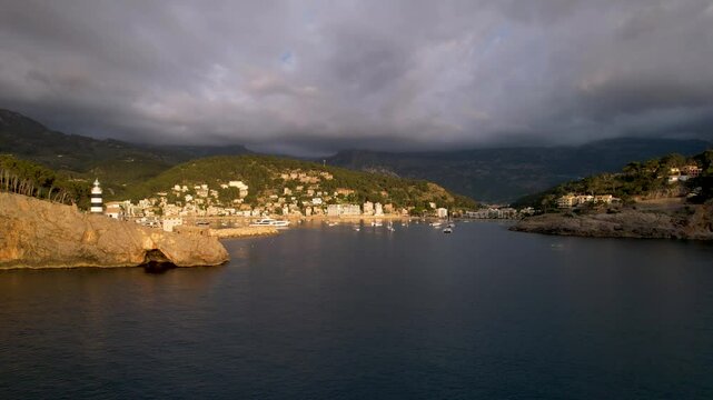 4K Aerial Drone video of popular summer destination, sunset over the cliffs with a lighthouse and a huge port of boats anchored at golden hour with seagulls flying. Port de Soller, Mallorca