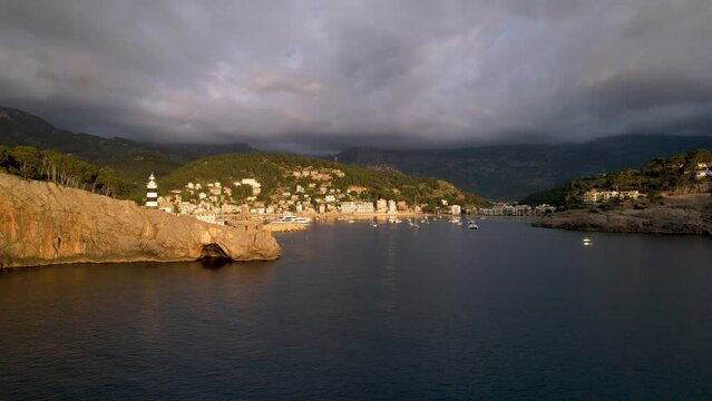 4K Aerial Drone video of popular summer destination, sunset over the cliffs with a lighthouse and a huge port of boats anchored at golden hour with seagulls flying. Port de Soller, Mallorca