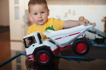 Cute little toddler plays with a toy dump truck in a home setting, smiling and enjoying driving,...