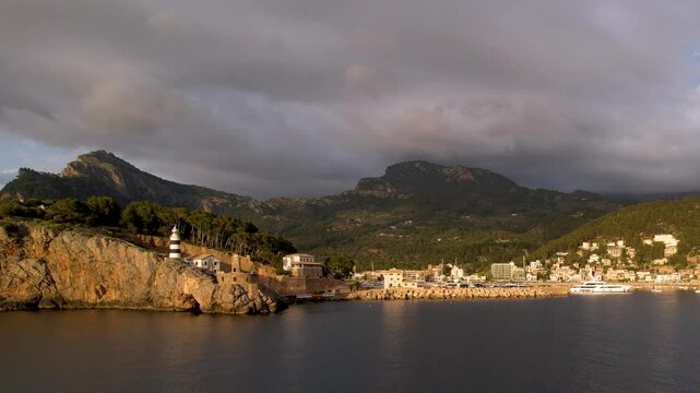 4K Aerial Drone video of popular summer destination, sunset over the cliffs with a lighthouse and a huge port of boats anchored at golden hour with seagulls flying. Port de Soller, Mallorca