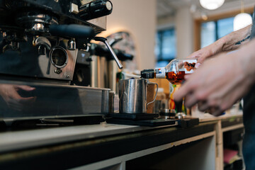Cropped shot of unrecognizable barista male adding sweet flavoured syrup in cappuccino coffee in mug cup. Closeup of barkeeper adding subtle sweetness to favorite cup of coffee is delicious.