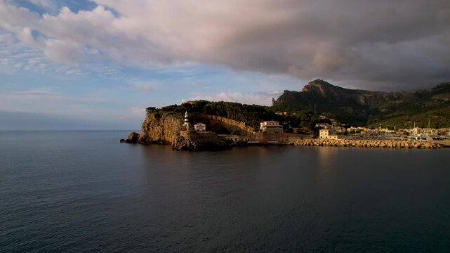 4K Aerial Drone video of popular summer destination, sunset over the cliffs with a lighthouse and a huge port of boats anchored at golden hour with seagulls flying. Port de Soller, Mallorca