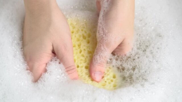 Female hand with a natural bath sponge squeezeing foam from the sponge. Woman holding shower sponge with soap suds. SPA concept.